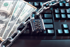 Ransomware concept: US hundred-dollar bills behind a chain and padlock on a computer keyboard (AI-generated by DALL-E)